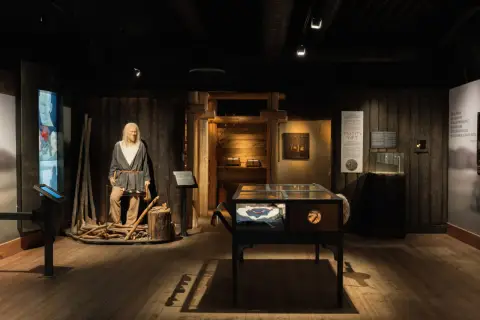 Vikingamuseum Stockholm: en vaxdocka av en viking med yxa, utställningsmontrar med föremål och informationstavlor.
