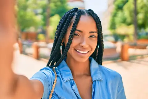 Sonrisa radiante de una mujer con distintos tipos de trenzas africanas, luciendo un estilo moderno y seguro.
