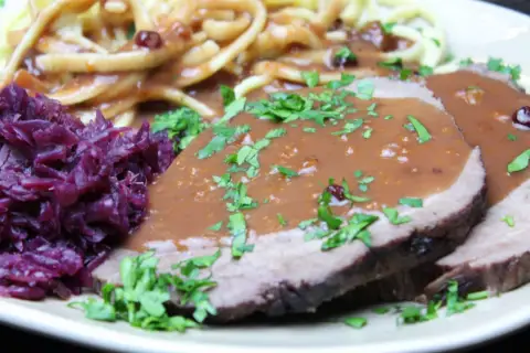 Sauerbraten einlegen rotwein: zarte Scheiben Fleisch in dunkler Soße, dazu Rotkohl und Nudeln.