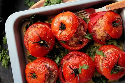 Six tomates farcies dorées, garnies d'une farce savoureuse et parsemées de persil frais, dans un plat de cuisson.