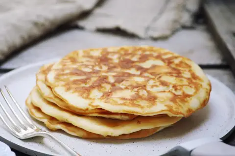 Stos puszystych, trzyskładnikowych placków bananowych na talerzu, obok srebrnego widelca. Idealne na śniadanie.