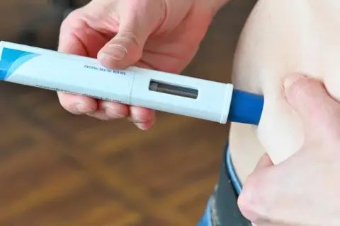 Eine Hand hält einen Aimovig-Injektor, bereit zur Anwendung.
