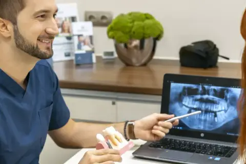 Dentysta omawia z pacjentką prawidłowe czyszczenie dziąseł, pokazując model zębów i zdjęcie rentgenowskie.