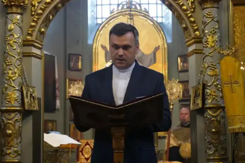 Duchowny w kościele polskokatolickim czyta z księgi. Różnice między kościołem polskokatolickim a rzymskokatolickim są widoczne w wystroju.