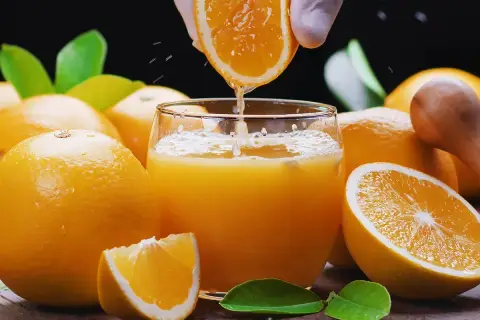 Un vaso de zumo de naranja recién exprimido, rodeado de naranjas frescas. ¡Cuidado! el zumo de naranja engorda si se abusa de él.