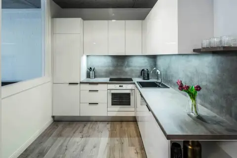 Nowoczesna kuchnia z białymi frontami i betonowym backsplash. Wygodny układ i funkcjonalne rozwiązania, idealne do planowania remont kuchni koszt.