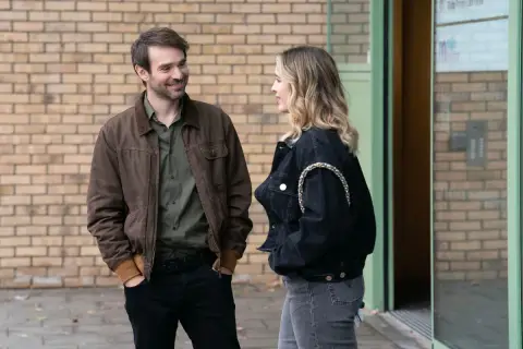 Man och kvinna pratar utanför en byggnad, kanske en scen från en svensk kin serie.
