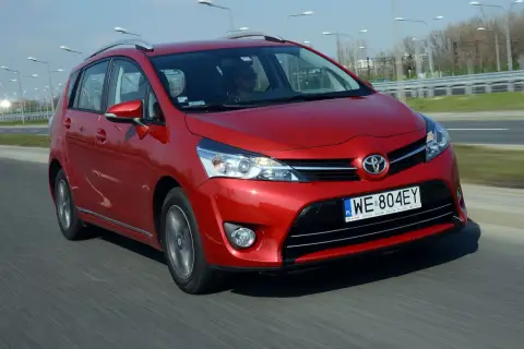 Czerwona Toyota Corolla Verso jedzie po drodze. Kierowca w okularach przeciwsłonecznych prowadzi auto.