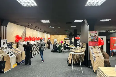 Wnętrze salonu z wystawionymi panelami podłogowymi, dekoracjami z balonów i ludźmi.