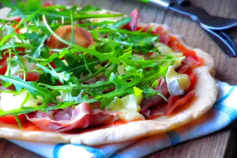 Pyszna pizza parma z rukolą i serem na drewnianym blacie.