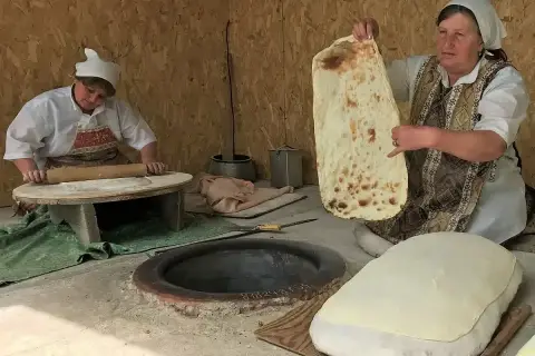 Kobieta pokazuje, co to jest lawasz – tradycyjny ormiański chleb. Obok druga kobieta wałkuje ciasto.