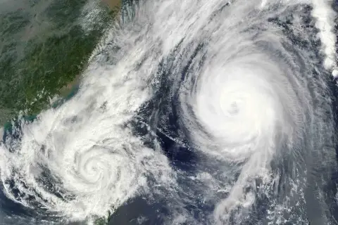 Dwa potężne wiry chmur, niczym oczy cyklonu, tworzą groźny **tajfun** nad oceanem, zbliżając się do zielonego wybrzeża.