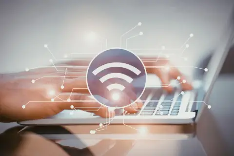Dłonie piszące na laptopie, symbol Wi-Fi i schemat połączeń. Dowiedz się, jak sprawdzić pasmo Wi-Fi w telefonie.
