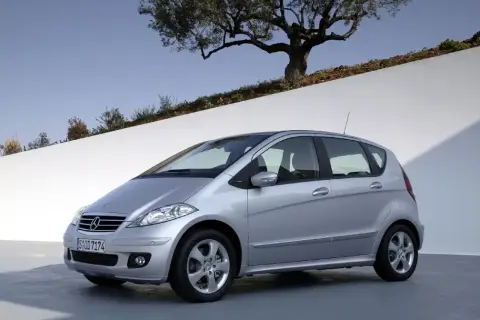 Srebrny Mercedes W169 stoi na tle białej ściany i drzewa oliwnego.