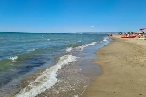 Plage de Fregene, mer bleue, sable doré, parasols et baigneurs profitant du soleil.