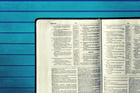 Otwarta Biblia z tekstem w języku angielskim na tle niebieskich desek.