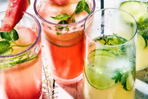Trois verres de cocktail classique, garni de concombre, menthe et pastèque, sur un fond clair.