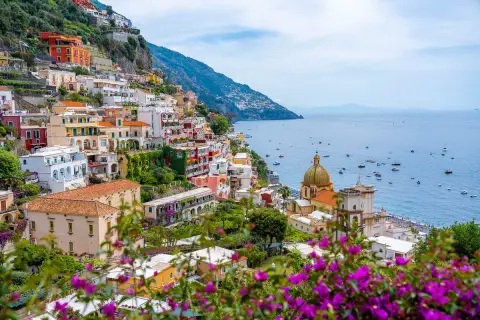 Colorful buildings cascade down a cliffside along the Amalfi road, overlooking a sparkling blue sea dotted with boats.