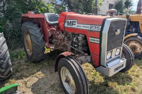 Czerwony Massey Ferguson 235 z napisem "Ursus" na masce, gotowy do pracy na polu.