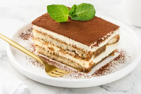 Pyszny kawałek tiramisu z mascarpone, posypany kakao i udekorowany miętą. Idealny sprawdzony przepis na deser.