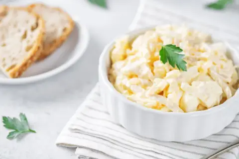 Kremowa, pyszna najlepsza sałatka z kalafiora, udekorowana natką pietruszki, obok kromek chleba.