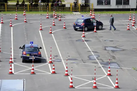 Plac manewrowy kat B. Dwa samochody z literą L na dachu i pachołki wyznaczają trasę egzaminu na prawo jazdy.
