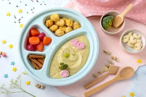 Kolorowy talerzyk z jedzeniem dla malucha: puree z warzyw, marchewka, maliny, chrupki i brokuł. Idealny na blw pierwszy posiłek.