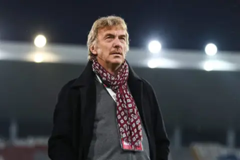 Zbigniew Boniek w płaszczu i szaliku na tle stadionu.