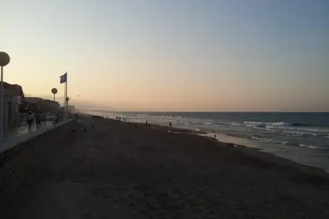 Gente pasea por la **playa de Piles** al atardecer, con el mar y el cielo en tonos pastel.