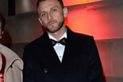 Kamil Nożyński z partnerką na ściance. Elegancki garnitur i czerwona sukienka.