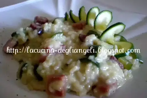 Risotto cremoso con robiola e speck croccante, guarnito con zucchine fresche. Un piatto delizioso e invitante.