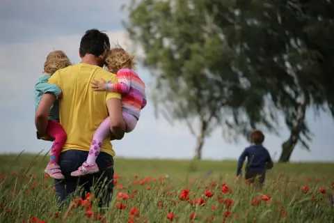 Un padre porta in braccio le sue due figlie in un campo di papaveri, un'immagine che cattura la psicologia del rapporto padre e figlia.