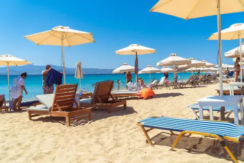 Słoneczny dzień na plaży Naxos. Leżaki pod parasolami, turkusowa woda i góry w tle.