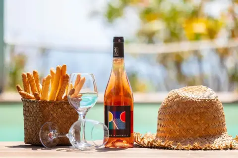 Un bicchiere di vino dolce dell'Elba, grissini croccanti e un cappello di paglia, perfetti per un aperitivo al mare.