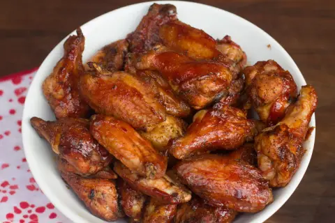 Un bol rempli d'ailes de poulet fumé, nappées d'une sauce brillante et caramélisée, prêtes à être dégustées.