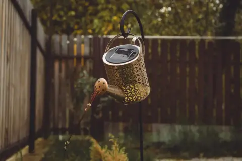 Ozdobna konewka z panelem solarnym, wisząca na haku. Czy lampa solarna ładuje się w cieniu?