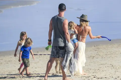 Chris Hemsworth z dziećmi i żoną na plaży. Rodzina cieszy się słońcem i piaskiem.