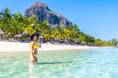 Frau im Bikini genießt das kristallklare Wasser an einem Traumstrand von Mauritius. Palmen und ein Berg im Hintergrund.