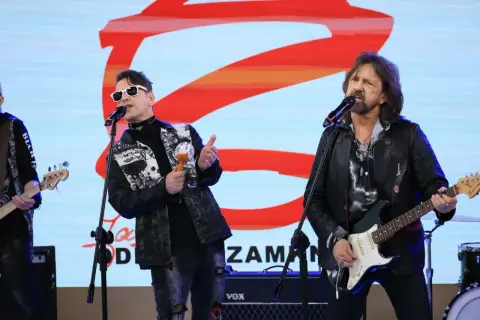 Zespół rockowy na scenie, wokalista w białych okularach i kolorowej kurtce, grający na marakasach. Obok gitarzysta w skórzanej kurtce. W tle logo "Jary Oddział Zamknięty".