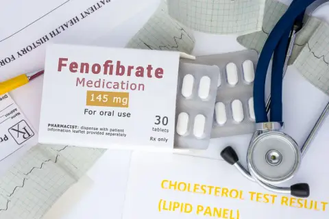 Opakowanie leku Fenofibrate 145 mg, tabletki, obok stetoskopu i wyników badań cholesterolu. Lipanthyl pomaga w leczeniu.