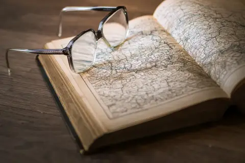 Okulary na otwartej księdze z mapą. Pomocne przy katalogowaniu źródeł i unikaniu błędów w researchu historycznym.
