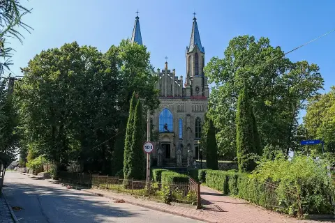 Neogotycki kościół w Krynkach, otoczony zielenią, z wieżami i charakterystycznym oknem.