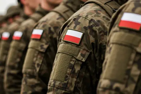 Żołnierze w mundurach moro z polskimi flagami na ramionach, gotowi na wezwania do wojska.