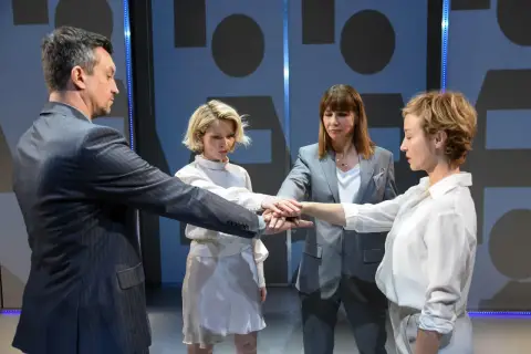 Cztery osoby łączą dłonie w geście jedności. To scena z nienasyceni spektakl, gdzie wspólnie budują coś ważnego.