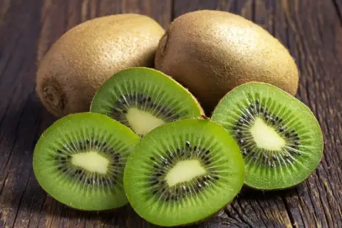 Kiwi na refluks. Dwa całe owoce kiwi i cztery przekrojone na pół, ukazujące zielony miąższ z czarnymi pestkami, leżą na drewnianym blacie.