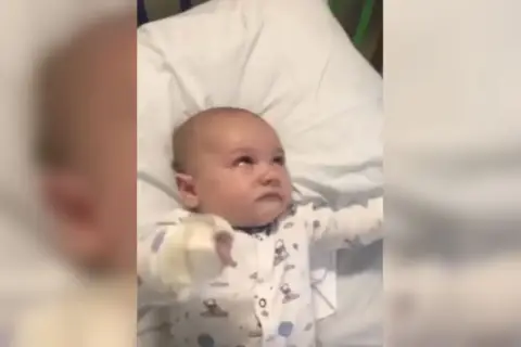 Bebé en pijama con patrones de nubes y lunas, con la mirada perdida, podría estar experimentando espasmos infantiles.