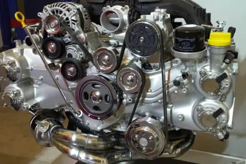 Błyszczący silnik Subaru z paskami, kołami pasowymi i filtrem oleju. Widać tu wiele elementów, w tym jeden duży cylinder.