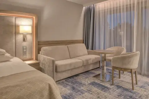 Przytulny pokój w hotelu 5 gwiazdkowym nad morzem: wygodna sofa, stolik z krzesłami i łóżko.