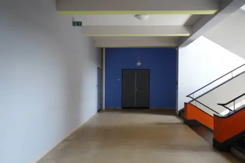 Ein Flur mit hellem Estrich, blauer Wand und auffälliger Treppe. Der Boden ist nach DIN-Norm verlegt.