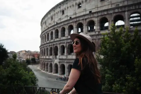 Une femme avec un chapeau et des lunettes de soleil admire le Colisée. Je visite Rome et ce moment est inoubliable.